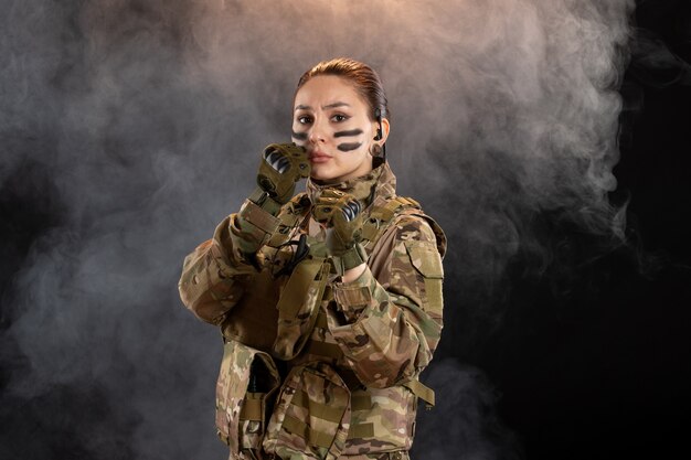 Vista frontale della soldatessa in mimetica sul muro scuro