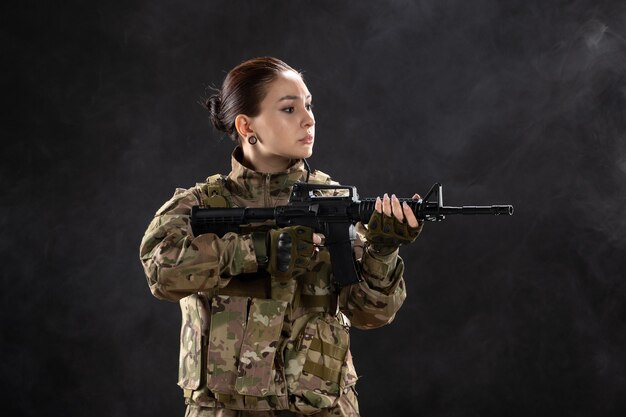 Vista frontale della soldatessa in uniforme che tiene il fucile sul muro nero