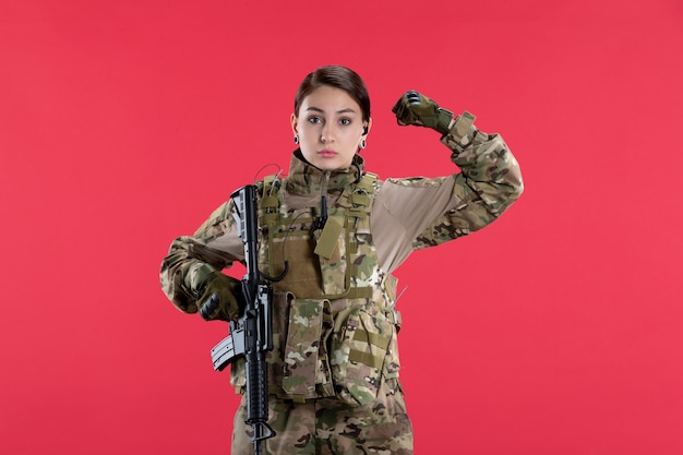 Vista frontale della soldatessa in uniforme militare con la parete rossa della mitragliatrice