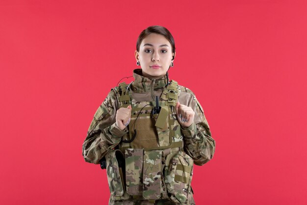 Vista frontale della soldatessa in uniforme militare sul muro rosso