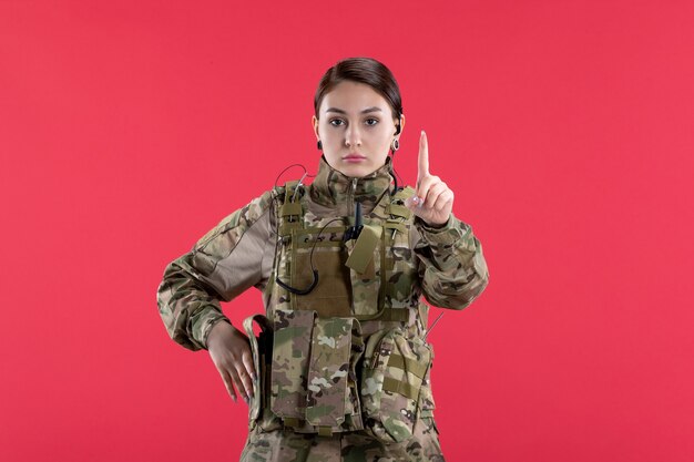 Vista frontale della soldatessa in uniforme militare sul muro rosso