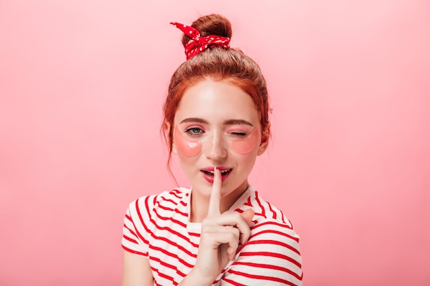 Vista frontale della splendida giovane donna con bende sugli occhi toccando le labbra con il dito. Lo studio ha sparato della ragazza adorabile che fa trattamento di cura della pelle e che mostra il segno segreto.