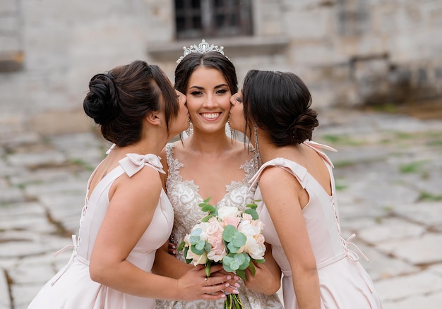 Vista frontale della sposa allegra che indossa in abito da sposa alla moda e corona sulla testa che tiene il mazzo di rose sorridente e alla ricerca