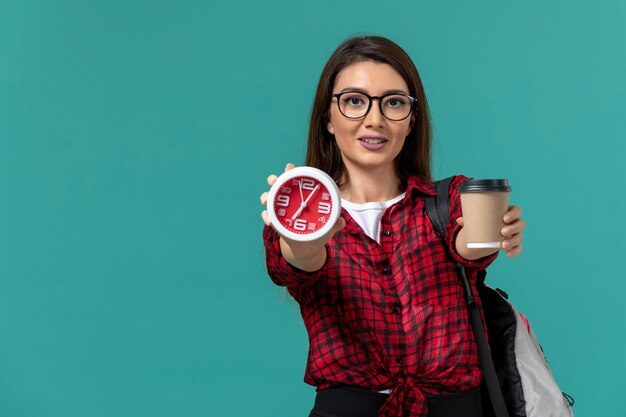 Vista frontale della studentessa che indossa uno zaino con orologi e caffè sulla parete blu