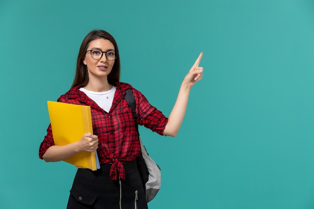 Vista frontale della studentessa che indossa uno zaino e che tiene i file sulla parete blu