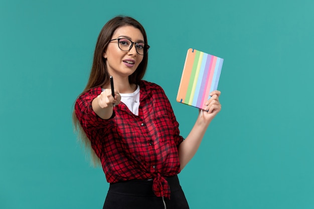 Vista frontale della studentessa in possesso di quaderno e penna sul muro azzurro