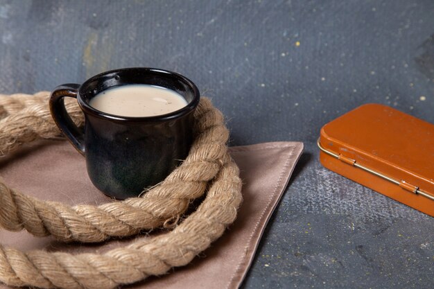 Vista frontale della tazza di latte con le corde sulla superficie grigia