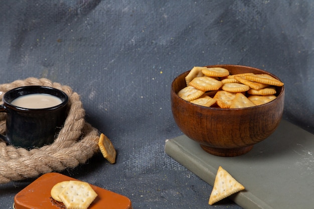 Vista frontale della tazza di latte con patatine e cracker sulla superficie grigia