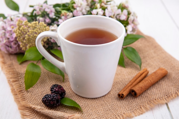Vista frontale della tazza di tè con cannella e fiori su un tovagliolo beige