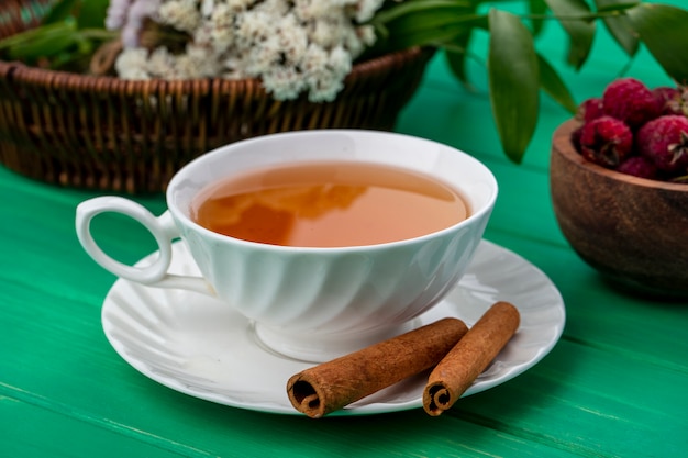 Vista frontale della tazza di tè con cannella e lamponi su una superficie verde