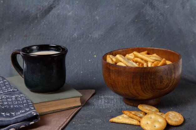 Vista frontale della tazza nera della tazza di latte con i cracker salati sulla superficie grigia