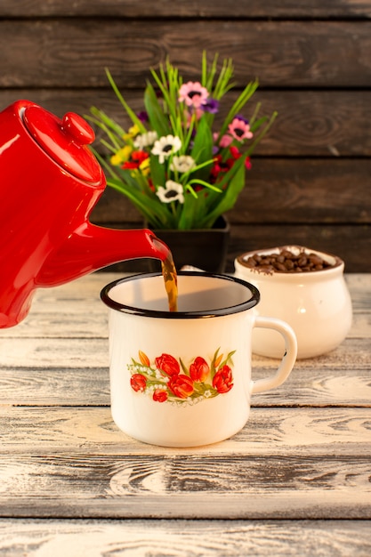 Vista frontale della tazza vuota con i semi e i fiori rossi del caffè marrone del bollitore sullo scrittorio di legno