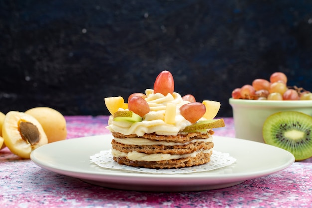 Vista frontale della torta crema con frutta fresca affettata sulla superficie scura