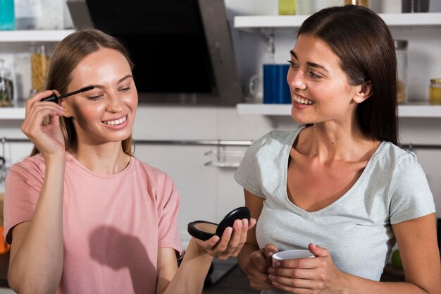 Vista frontale delle amiche a casa usando il mascara