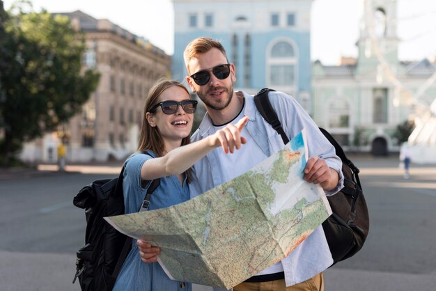 Vista frontale delle coppie turistiche che indicano a qualcosa mentre tenendo mappa