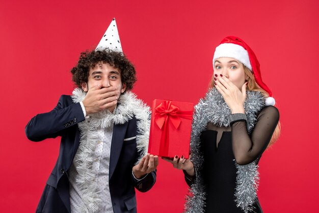 Vista frontale delle giovani coppie che tengono il nuovo anno presente sul muro rosso amore emozione natale