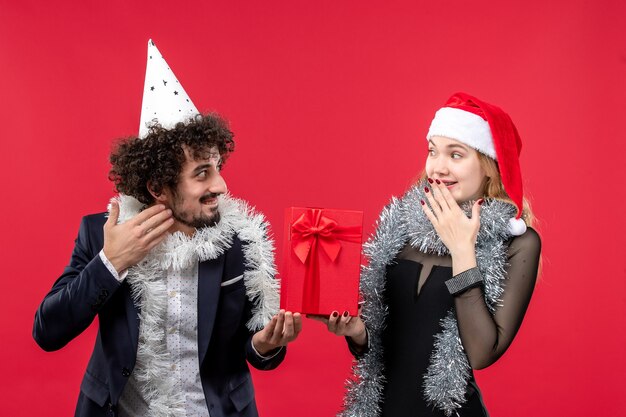 Vista frontale delle giovani coppie che tengono il nuovo anno presente sul muro rosso amore emozione natale