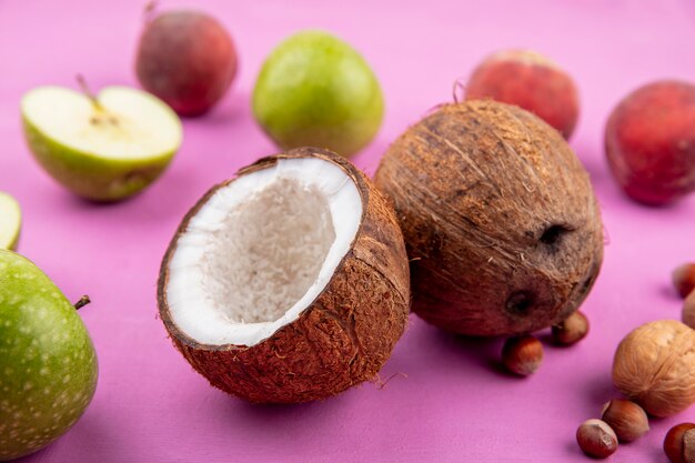 Vista frontale delle noci di cocco fresche con le pesche verdi delle mele su superficie rosa