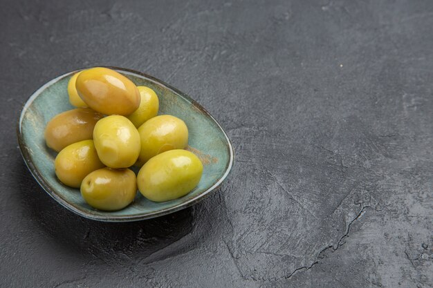 Vista frontale delle olive verdi organiche fresche su un piatto blu su un fondo nero