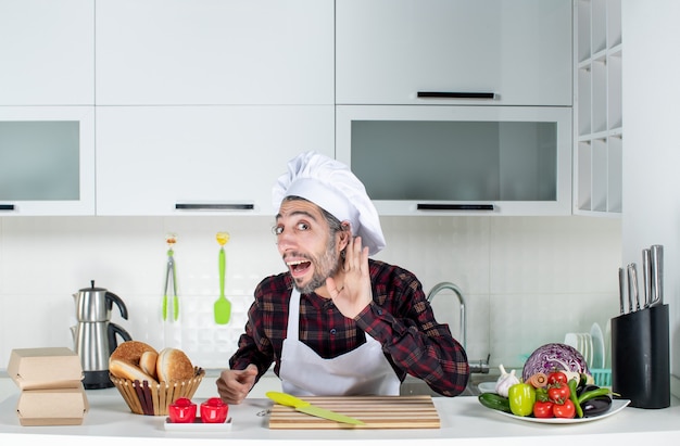 Vista frontale dello chef maschio che ascolta qualcosa in piedi dietro il tavolo della cucina in cucina