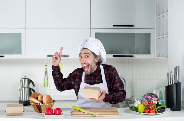 Vista frontale dello chef maschio che sorprende con un'idea che tiene in mano una scatola in cucina