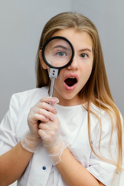 Vista frontale dello scienziato curioso della ragazza che per mezzo della lente d'ingrandimento