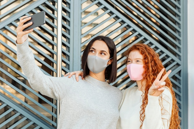 Vista frontale di amiche con maschere facciali all'aperto prendendo un selfie