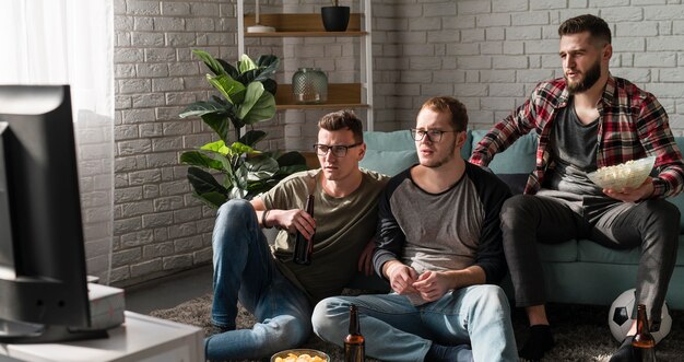 Vista frontale di amici maschi che guardano sport in tv con birra e calcio