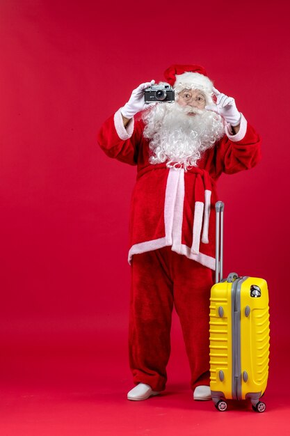 Vista frontale di Babbo Natale con borsa gialla che tiene la macchina fotografica sulla parete rossa