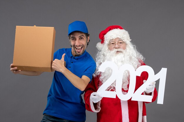 Vista frontale di Babbo Natale con corriere maschio che tiene la scatola di cibo e sul muro grigio