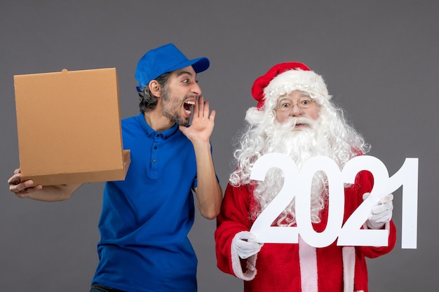 Vista frontale di Babbo Natale con corriere maschio che tiene la scatola di cibo e sul muro grigio