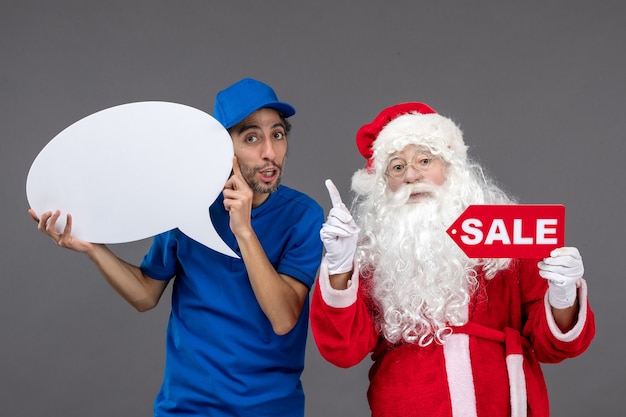 Vista frontale di Babbo Natale con corriere maschio che tiene segno bianco e banner di vendita sul muro grigio