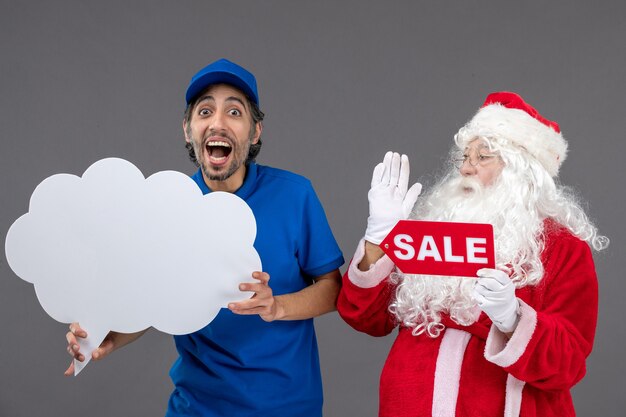 Vista frontale di Babbo Natale con corriere maschio che tiene segno di nuvola bianca e vendita sul muro grigio