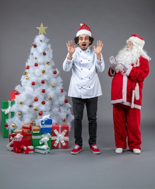 Vista frontale di Babbo Natale con cuoco maschio intorno a regali di Natale sul muro grigio