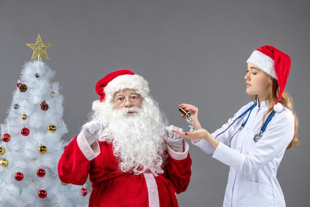 Vista frontale di Babbo Natale con dottoressa che sta versando pillole sul muro grigio