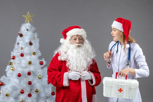 Vista frontale di Babbo Natale con giovane donna medico sul muro grigio
