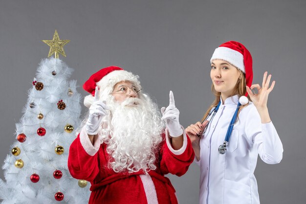 Vista frontale di Babbo Natale con giovane donna medico sul muro grigio