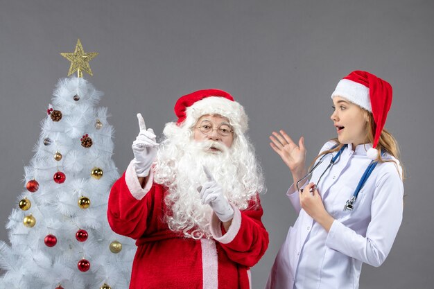 Vista frontale di Babbo Natale con giovane dottoressa su un muro grigio