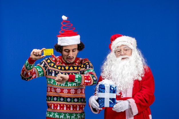 Vista frontale di babbo natale con il giovane che tiene la carta di credito e presente sul muro blu