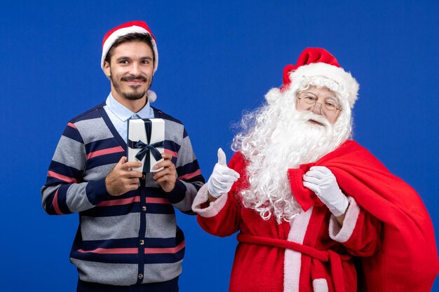 Vista frontale di babbo natale con il giovane che tiene presente sul muro blu