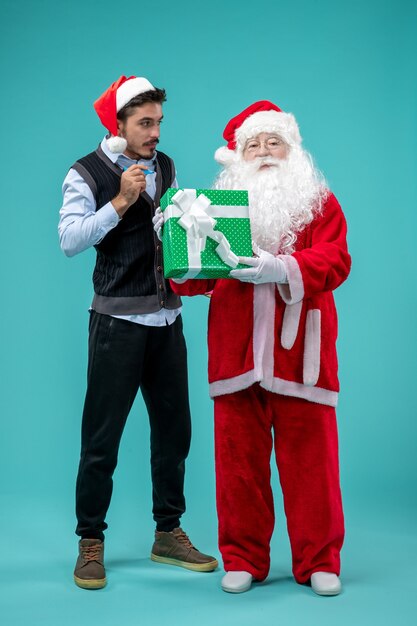 Vista frontale di Babbo Natale con il giovane e regalo di festa sulla parete blu