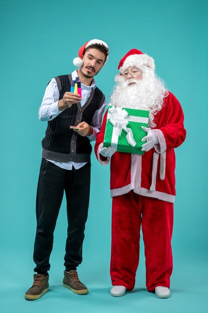 Vista frontale di Babbo Natale con il giovane e regalo di festa sulla parete blu