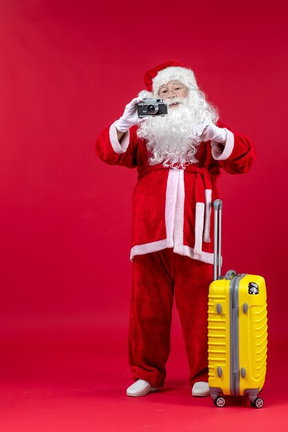 Vista frontale di Babbo Natale con il sacchetto giallo che cattura foto con la fotocamera sulla parete rossa