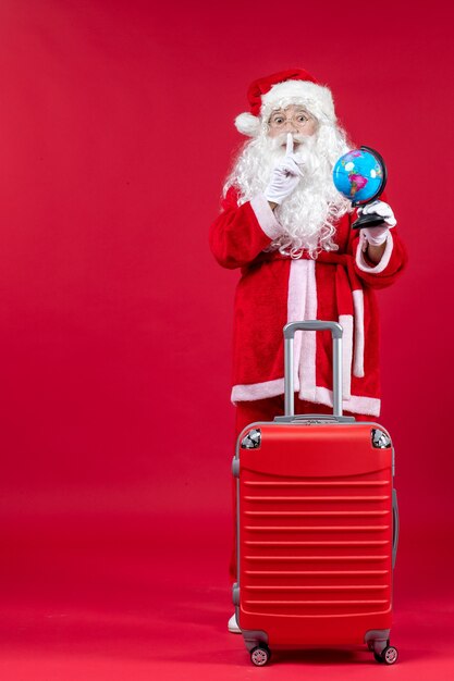 Vista frontale di Babbo Natale con la borsa che tiene un piccolo globo e si prepara per il viaggio sulla parete rossa