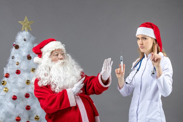 Vista frontale di Babbo Natale con la dottoressa che prepara l'iniezione sul muro grigio