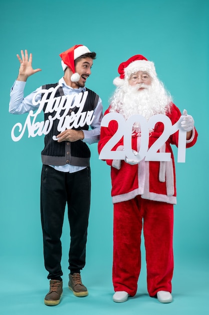 Vista frontale di Babbo Natale con maschio che tiene felice anno nuovo e 2021 tavole sulla parete blu