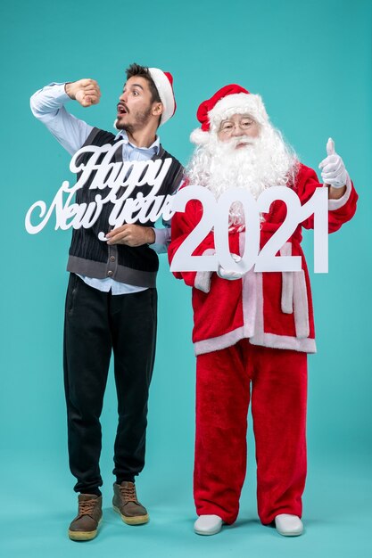 Vista frontale di Babbo Natale con maschio che tiene felice anno nuovo e 2021 tavole sulla parete blu