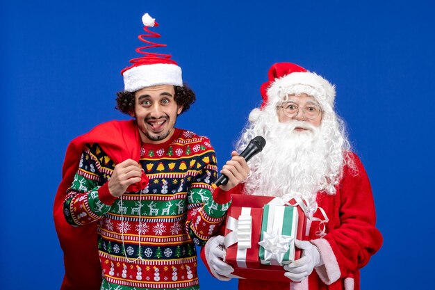 Vista frontale di babbo natale con un giovane che tiene il microfono sulla parete blu