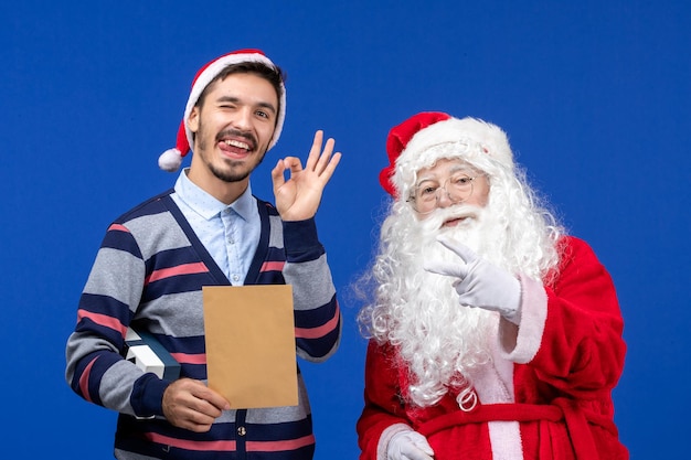 Vista frontale di babbo natale con un giovane che tiene in mano una lettera sul muro blu