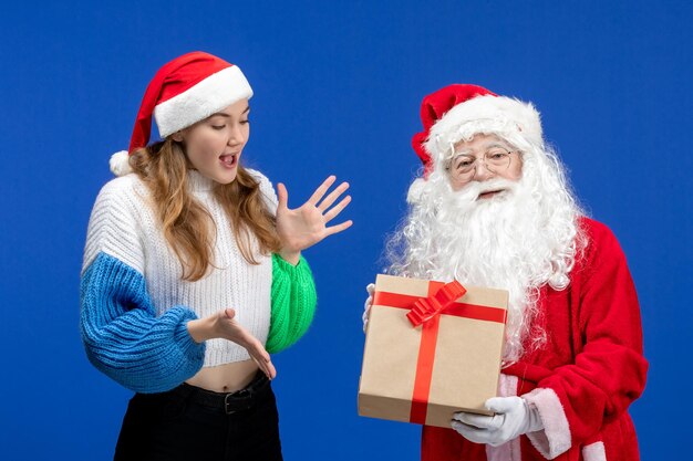 Vista frontale di babbo natale insieme alla donna che tiene presente sul muro blu